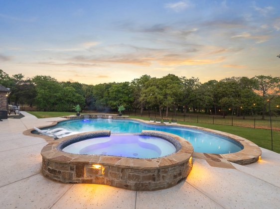 Freeform pool with elevated stone spa at sunset